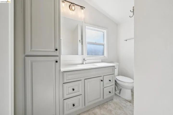 Bathroom featuring a light gray vanity with a white countertop and undermount sink, an overhead wall-mounted light fixture, and a built-in storage cabinet