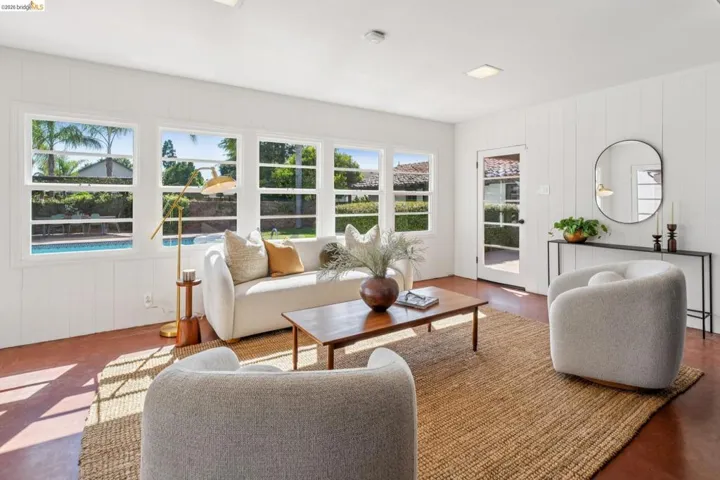 Bright living space featuring multiple windows overlooking a pool, a glass-paned door, white vertical paneled walls, recessed lighting, and rich red-toned flooring