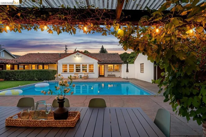 Expansive backyard patio featuring a built-in swimming pool, mature perimeter hedging, and a separate structure