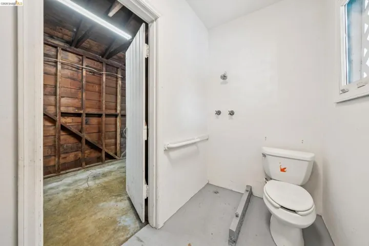 Utility space featuring a white toilet, wall-mounted faucet rough-ins, and a window with a decorative screen