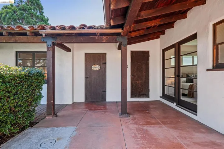 Covered patio featuring exposed wood beams, a terra cotta tile roof, and a red-hued concrete slab