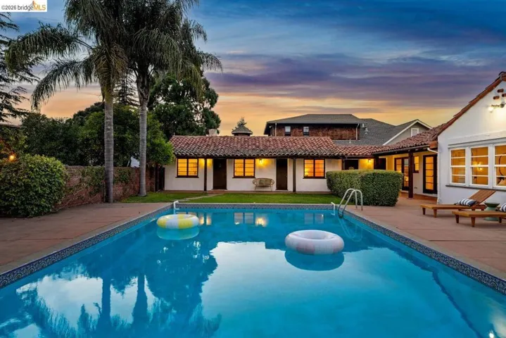 Expansive backyard featuring a rectangular swimming pool with integrated steps, surrounding hardscaping, mature palm trees, and manicured hedges
