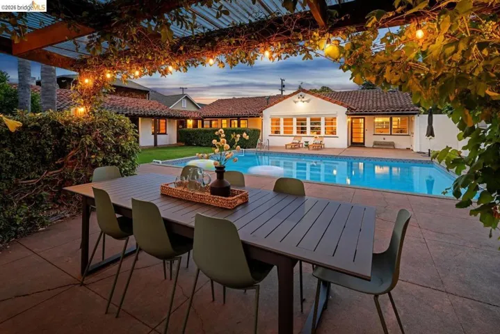 Patio dining area with a wood pergola, string lighting, and an expansive pool