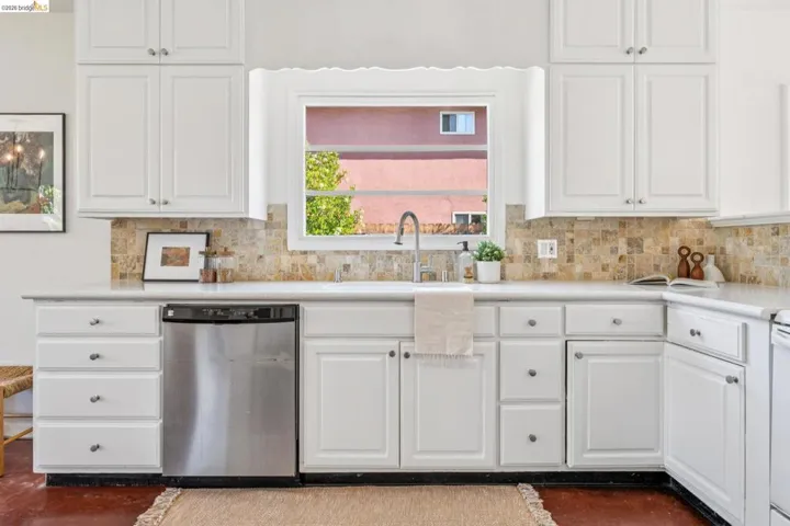 Kitchen featuring white cabinetry, a stainless steel dishwasher, a window over the sink, solid surface countertops, and a tile backsplash