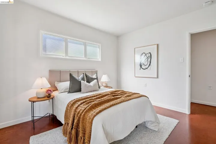 Bright bedroom featuring white walls, a multi-pane window with blinds, and rich, dark-toned flooring