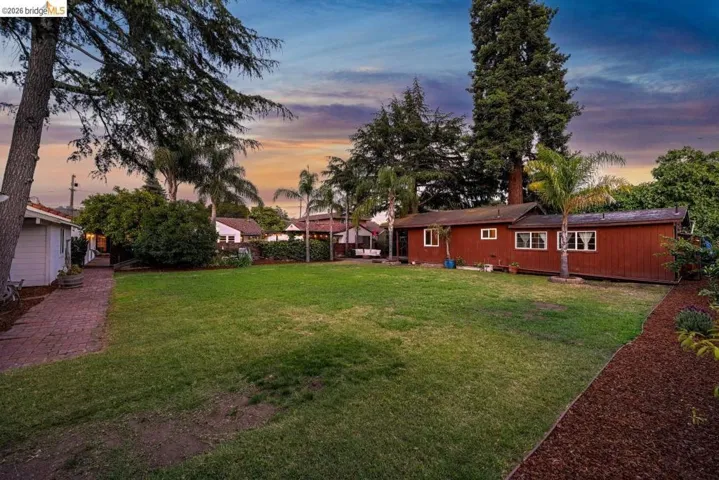 Expansive grassy yard area with a red exterior structure, surrounded by mature trees and landscaping