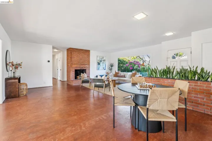 Open-concept living area featuring rich, warm-toned flooring, a brick fireplace, and a large front-facing window