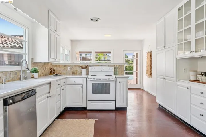 Bright kitchen featuring white cabinetry, a stone tile backsplash, and a farmhouse sink