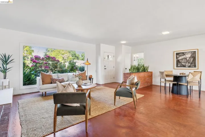 Bright living space featuring a large picture window, red-toned concrete flooring, a brick planter, and a white entry door with frosted glass