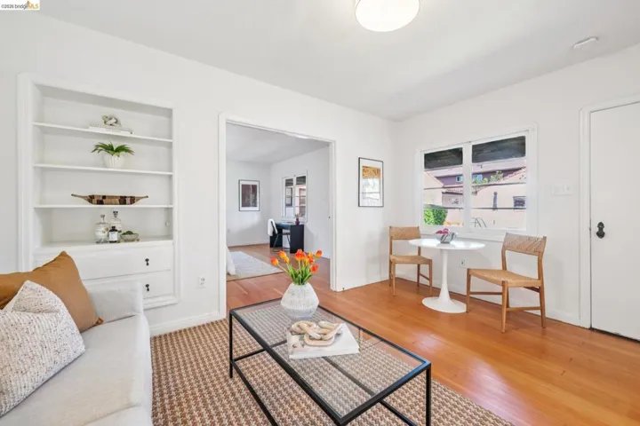 Living area featuring light wood-finish flooring, recessed built-in shelving with lower cabinetry, a white ceiling light fixture, and a window with white trim