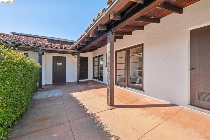 Covered walkway featuring exposed wood beams, white stucco walls, and terracotta tile roofing