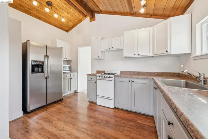 Kitchen featuring a vaulted wood-finish ceiling with track lighting, stainless steel side-by-side refrigerator, white upper cabinetry, grey lower cabinetry, and wood-finish flooring