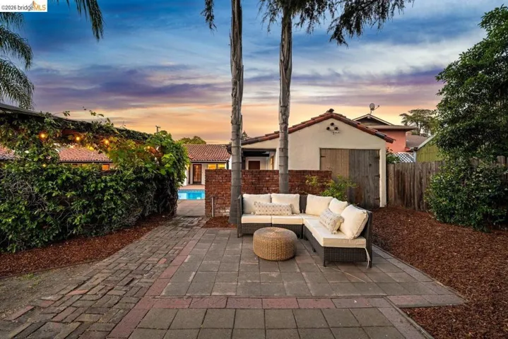 Expansive brick paver patio with a separate pool area, mature palm trees, and a detached structure featuring a clay tile roof