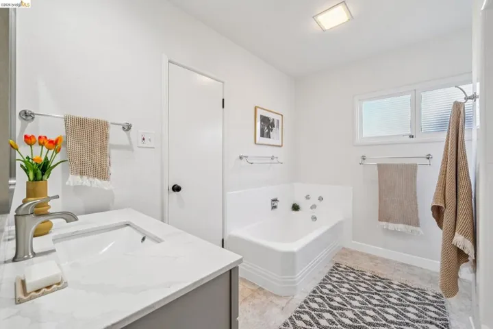 Bathroom featuring a built-in tub with chrome fixtures, a single vanity with a quartz-look countertop, an integrated rectangular sink, and a brushed nickel faucet