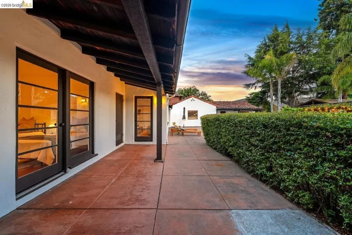 Spacious patio featuring terra cotta-toned concrete flooring, a white stucco exterior, and dark wood eaves