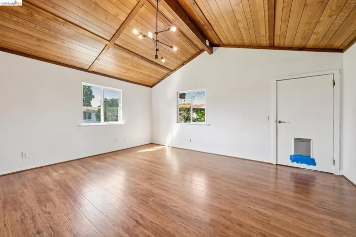 Vaulted wood-paneled ceiling with exposed beams, wood-finish flooring, two windows with exterior views, and a contemporary light fixture