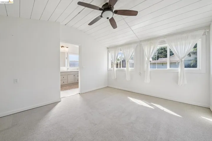 Carpeted interior space featuring a vaulted tongue-and-groove ceiling, multiple windows, and an overhead ceiling fan
