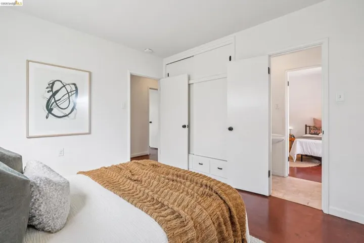 Bedroom featuring dark wood-finish flooring, white walls, and built-in closet cabinetry with bottom drawers