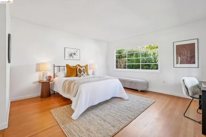 Bright bedroom featuring wood-finish flooring, a large multi-pane window, and white walls