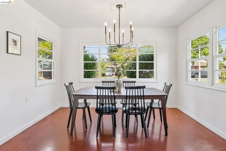 Bright interior space featuring multiple windows with white trim, a dark-toned chandelier, and rich red-toned flooring