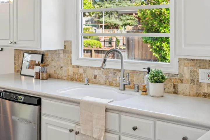 Kitchen sink area featuring a stainless steel faucet, a white undermount sink, and light-toned solid surface countertops
