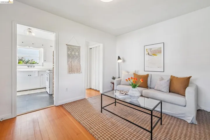 Bright living space featuring hardwood flooring, white walls, and a large doorway leading to a kitchen with white cabinetry and a window