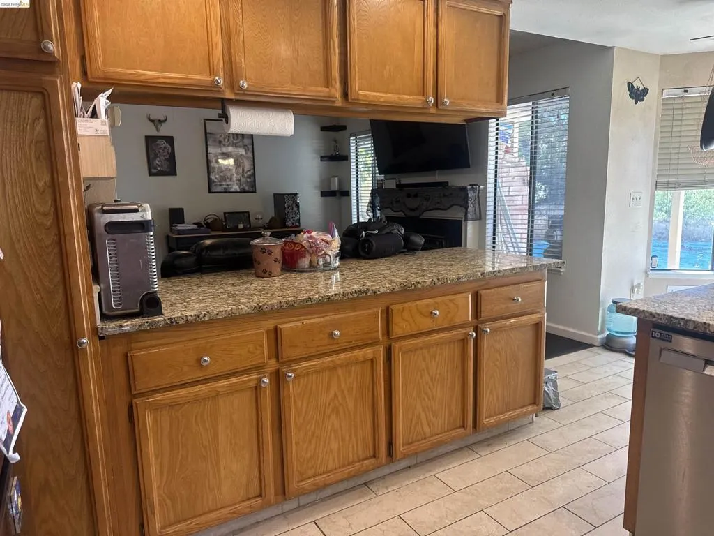 Kitchen featuring wood cabinetry, light-toned granite-style countertops, and tile flooring