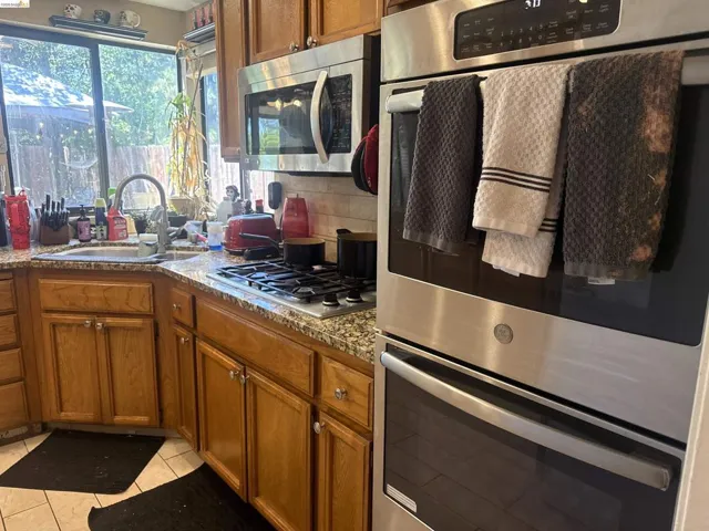 Kitchen featuring stainless steel double ovens, a built-in microwave, wood cabinetry, granite countertops, and a gas cooktop