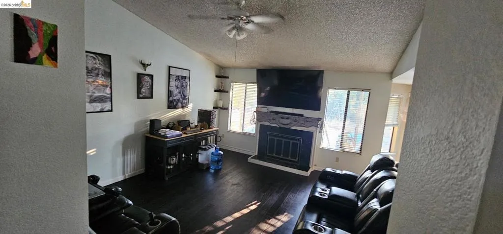 Living area with dark wood-finish flooring, vaulted ceilings, and a ceiling fan