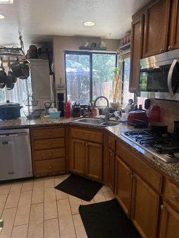 Kitchen featuring light wood cabinetry, granite-style countertops, stainless steel appliances, a gas range, and tile flooring