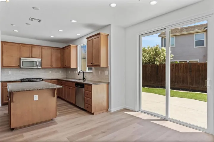 Kitchen featuring wood-finish cabinetry, stainless steel appliances, a center island with a stone countertop, and a tiled backsplash