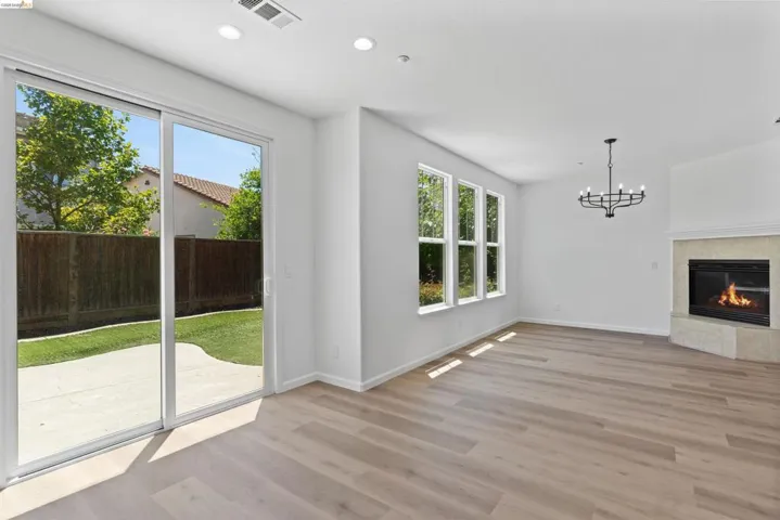 Open-concept living area featuring light wood-finish flooring, a stone-surround fireplace, and a contemporary chandelier