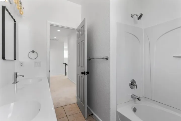 White bathroom featuring a dual-sink vanity with chrome fixtures and a tub-shower combination