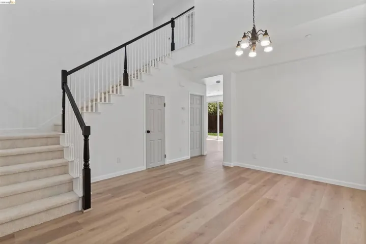 Two-story interior featuring a carpeted staircase with white risers and a black handrail, light wood-finish flooring, white walls, and a chandelier with five sconces