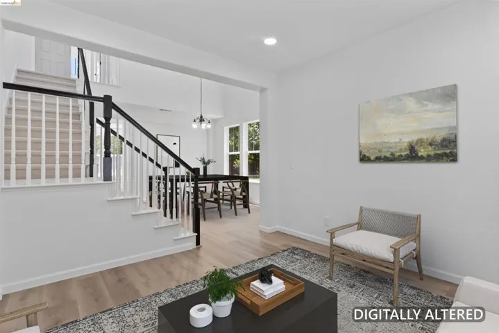 Open-concept living area featuring light wood-finish flooring, white walls, a black and white staircase with carpeted treads, and a dining space with multiple windows