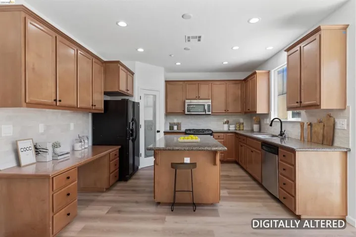 Spacious kitchen featuring light wood cabinetry with black hardware, an island with countertop seating, stainless steel appliances, and wood-finish flooring