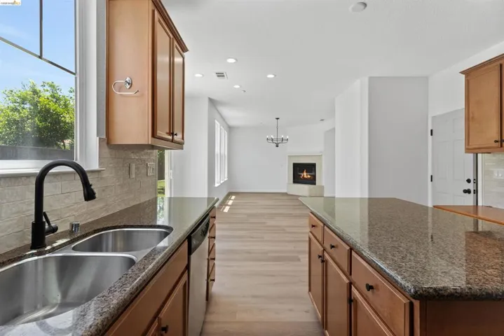 Kitchen featuring granite countertops, wood-finish cabinetry, a double basin stainless steel sink with a black gooseneck faucet, and a tile backsplash