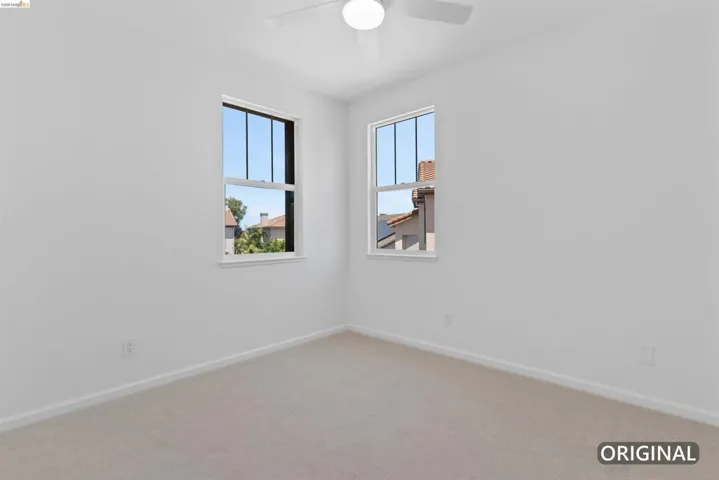 Bright room featuring two double-hung windows, neutral-toned carpeting, white baseboards, and a ceiling fan with integrated lighting