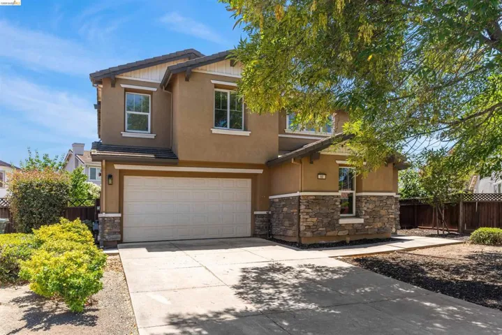 Two-story stucco residence featuring a two-car garage, stone veneer accents, and a concrete driveway