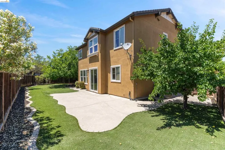 Expansive rear patio featuring a concrete surface, artificial turf, and a perimeter fence
