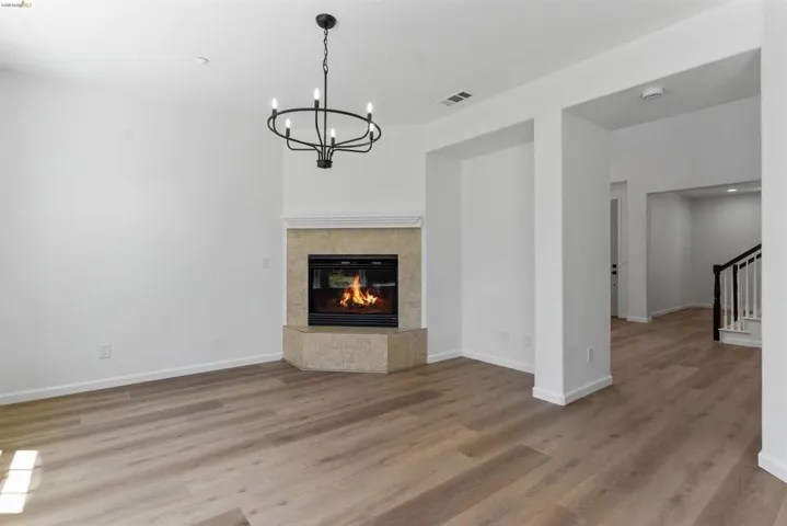Living area featuring a corner fireplace with a stone surround and mantel, wood-finish flooring, and a black chandelier