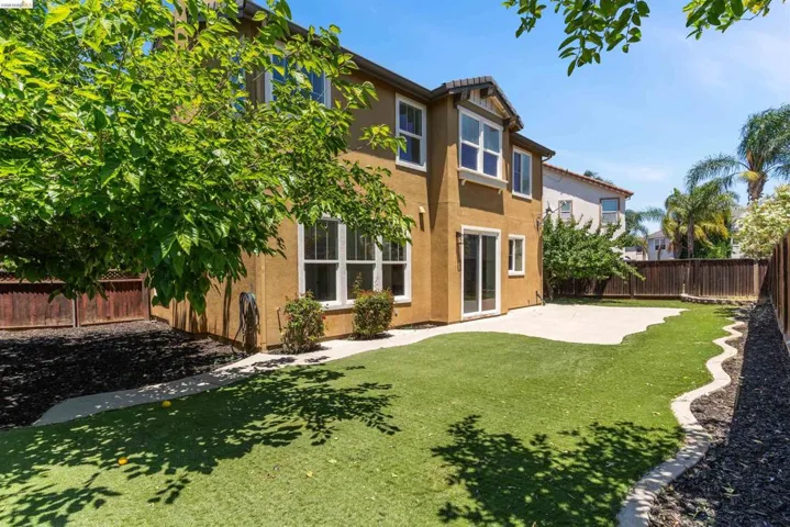 Spacious backyard featuring an artificial turf lawn, concrete patio, and dark wood fencing
