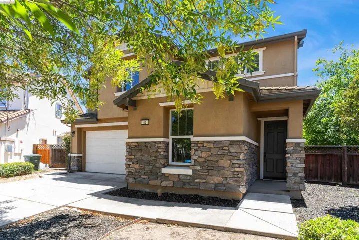 Two-story stucco exterior featuring a stone facade, covered entry, attached garage, and a concrete driveway