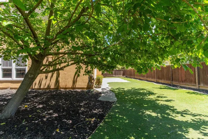Expansive backyard featuring artificial turf, a concrete pathway, and a perimeter wood fence