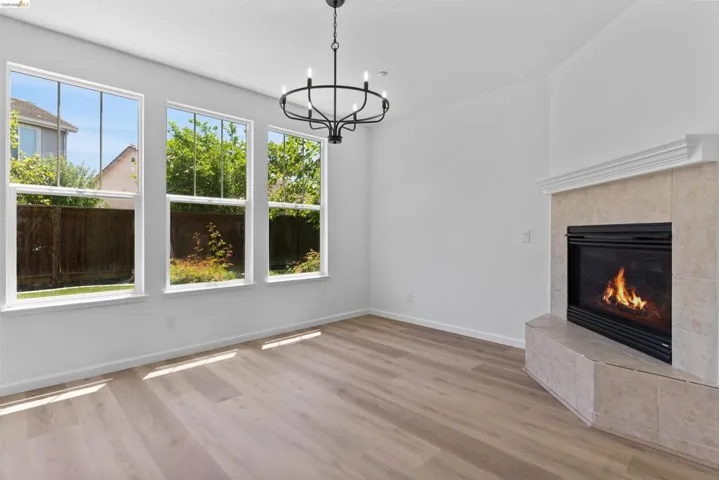 Living area featuring wood-finish flooring, a contemporary chandelier, three expansive windows, and a tiled fireplace with a classic mantel