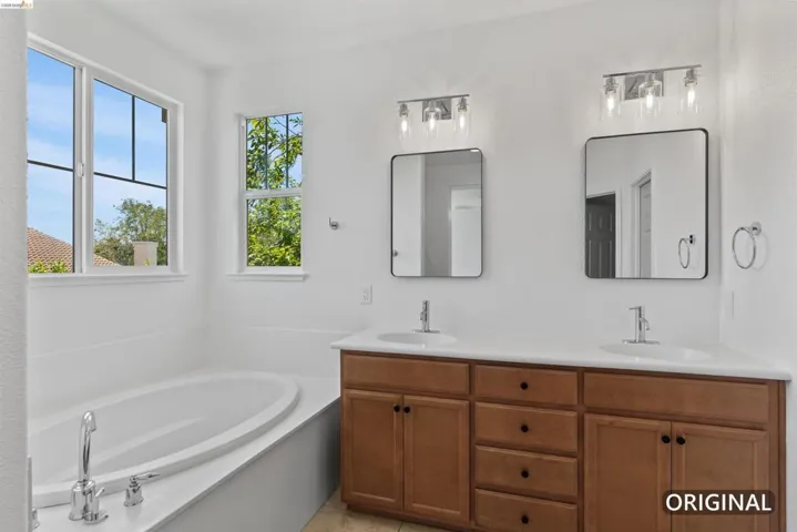 Bathroom with a built-in soaking tub, dual windows, and an extended vanity featuring two sinks