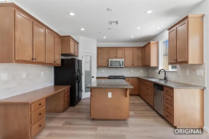 Open-concept kitchen featuring light wood-finish cabinetry, a central island, stainless steel appliances, and wood-finish flooring