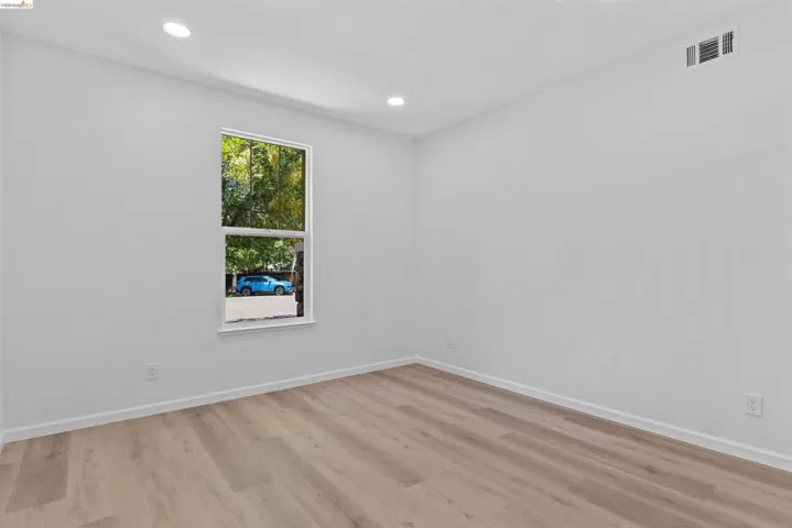 Room featuring new wood-finish flooring, recessed lighting, and a window with white trim