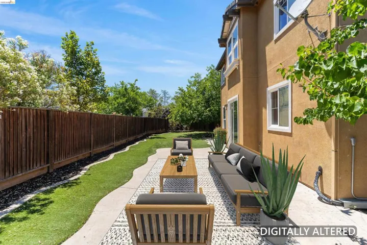 Spacious backyard featuring a stucco exterior, concrete patio with decorative stone inlay, a long privacy fence, and a manicured lawn