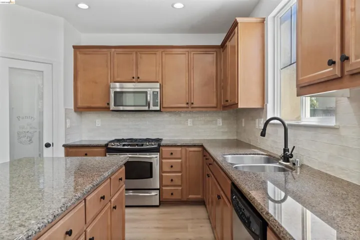 Kitchen featuring wood cabinetry, stainless steel appliances, granite countertops, tile backsplash, and a double basin sink with a black gooseneck faucet